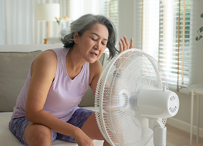 A middle-aged woman in shorts and a tank top cools down in front of a white fan